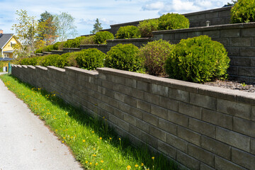 Garden landscape design. Decorative wall made of dark gray stone blocks or concrete cement bricks....