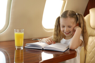 Cute little girl reading book at table in airplane during flight