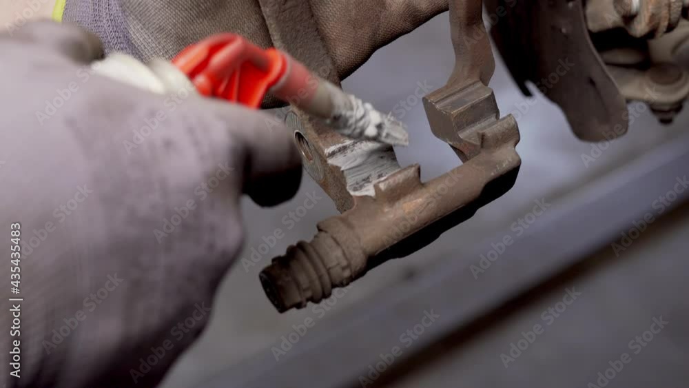 Poster applying copper paste to brake caliper mount with a small brush to avoid rust and corrosion. close u