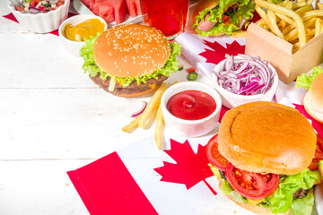 Set of various Canada Day bbq food. Picnic party table with maple leaf shaped watermelon, flags, burgers, hot dogs, fries and sauces, cold drinks, white table with red decor, top view copy space
