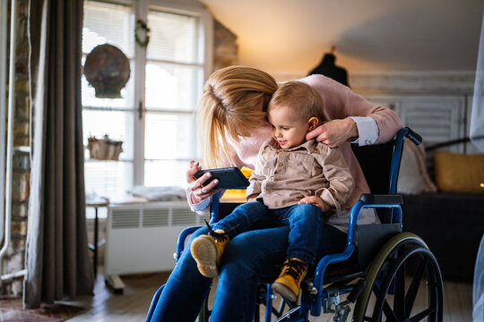 Happy smiling mother with disability in wheelchair playing with child at home