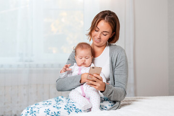 A mother holds a sleeping child in her arms and shows him something on her smartphone. Close-up portrait. Home interior