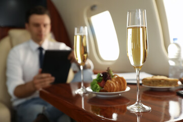 Businessman working at table in airplane during flight, focus on glass of champagne - obrazy, fototapety, plakaty