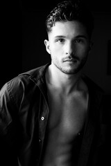 Portrait of attractive young man with stubble and open shirt revealing defined pecs and abs looking at camera.