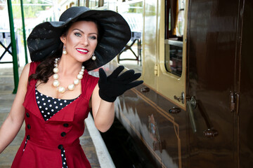 Fototapeta na wymiar Beautiful woman in vintage red polka dot dress standing on vintage railway platform.