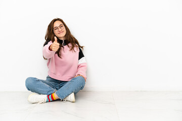 Young caucasian woman sitting on the floor isolated on white background with thumbs up because something good has happened