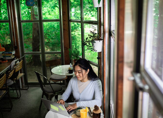 Young Asian woman working in coffee shop using laptop.