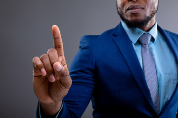 Mid section of african american businessman touching invisible screen against grey background