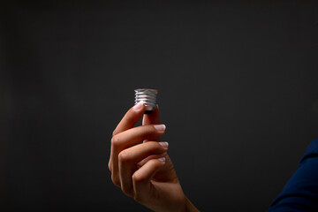 Close up of hand holding bulb screw base against black background