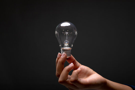 Mid section of businesswoman holding a light bulb against black background