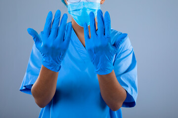Mid section of female surgeon wearing surgical gloves against grey background