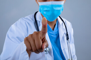Mid section of doctor wearing face mask touching invisible screen against grey background - Powered by Adobe