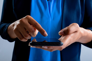 Fototapeta premium Mid section of businesswoman using a smartphone against grey background