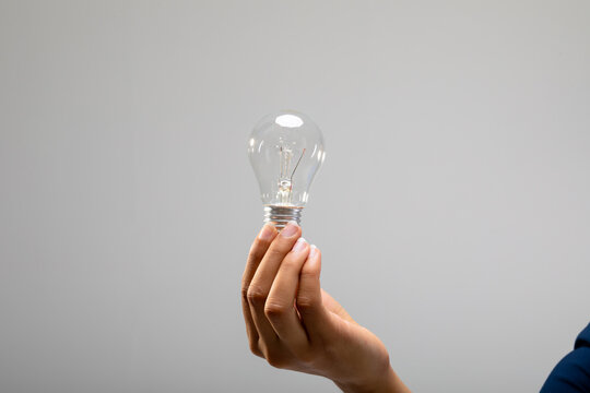 Close up of person holding a light bulb against grey background
