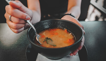 Woman hand eating chicken soup in black bowl sitting in cafe