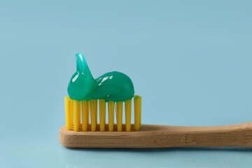 Wooden brush with toothpaste on light blue background, closeup