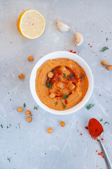 Flat lay of a bowl of delicious hummus with olive oil, garlic and paprika on a grey background.