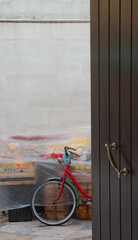 a front detail of a red bicycle in front of a nylon covered groceries, behind an open door in Bari, Italy