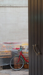 a front detail of a red bicycle in front of a nylon covered groceries, behind an open door in Bari,...