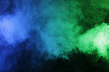 Artificial magic smoke in blue green light on black background