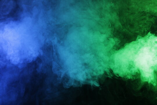 Artificial magic smoke in blue green light on black background