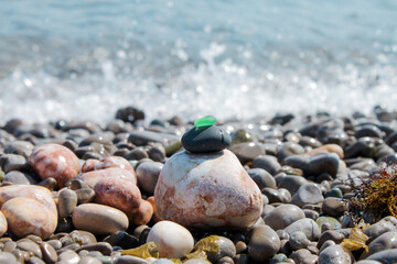 Fototapeta na wymiar The pyramid is built on a pebble beach of sea pebbles with a matte smooth green glass at the top. Against the background of waves, water splashes and foam