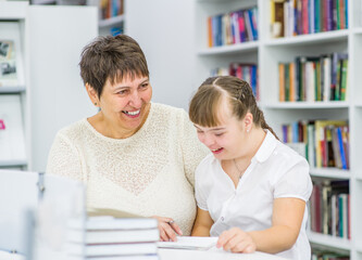 Happy teacher and girl with syndrome down read a book at library. Education for disabled children concept