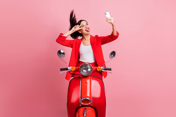 Fototapeta na wymiar Photo of young funky funny smiling cheerful girl riding moped take selfie on phone show v-sign isolated on pink color background