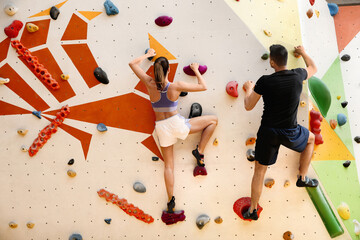 Athletic man and woman climbing wall in gym, back view