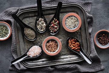 Various spices in ceramic oriental spoons and pinch bowls on dark vintage metal tray. Textile towel...