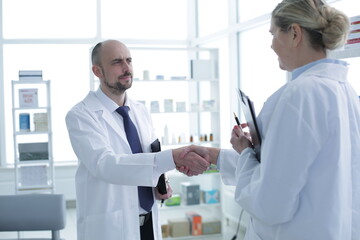 Pharmacists is Working. Man and Woman Handshaking with Each Other. Persons is Smiling. People Wearing Special Medical Uniform. People Located in Pharmacy.