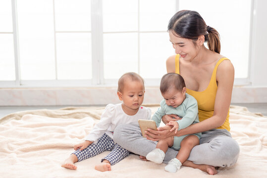 Young Asian beautiful mother watching a photo or video clip from mobile phone with 2 little children. Mother having a happy time with her babies.