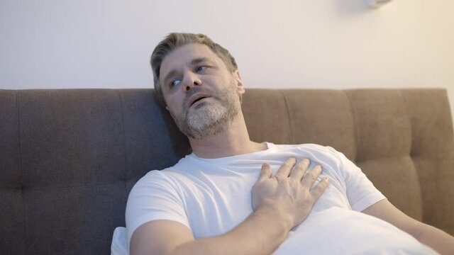 Man in his 50s suffering from chest pain, lying in bed, breathing heavily