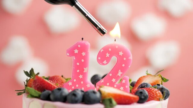 Birthday cake candle number 12. Candle and cake on pink background and fire by lighter. Close-up and slow motion