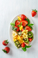 Colorful ripe fruits and berries on platter, top view on white background. Vegetarian food concept. Strawberry, kiwi, apple and oranges.