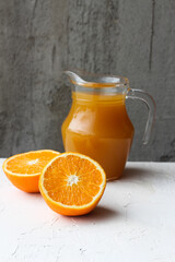 Minimalistic concept of healthy food. Fresh orange juice in the glass jug and juicy fresh oranges on a neutral vertical background