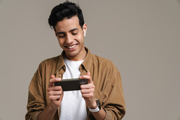 Brunette hispanic man smiling while using cellphone and earphones