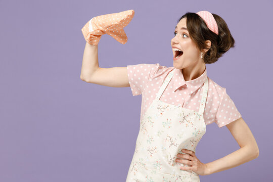 Young amazed excited happy cheerful fun housewife housekeeper chef cook baker woman in pink apron play talk with potholder isolated on pastel violet background studio portrait. Cooking food concept.