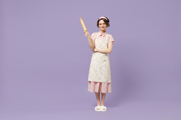 Full length smiling young happy housewife housekeeper chef cook baker woman in pink apron hold rolling pin stand look camera isolated on pastel violet background studio Cooking food process concept