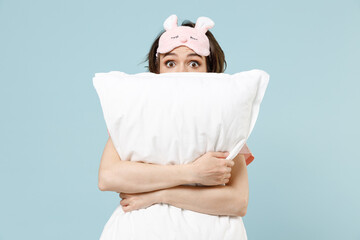 Young scared shocked caucasian woman in pajamas jam sleep eye mask rest relax at home look camera hug pillow isolated on pastel blue color background studio portrait Bad mood night bedtime concept