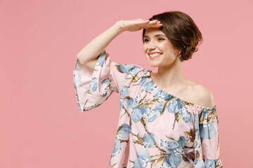 Obraz premium Young smiling happy caucasian woman 20s with short hairdo wear trendy blouse hold hand at forehead look far away distance isolated on pastel pink background studio portrait. People lifestyle concept.