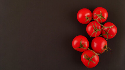 Fresh cherry tomatoes on a black background with spices. Top view with copy space.