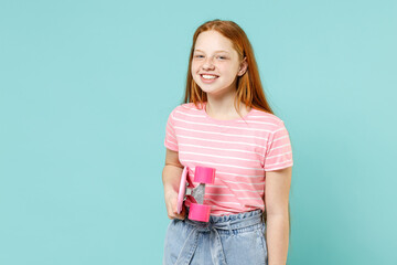 Little redhead kid girl 12-13 years old in pink striped t-shirt hold skateboard rest on summer vacations leisure time isolated on pastel blue background studio. Children lifestyle childhood concept.