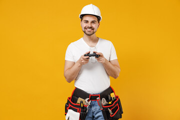 Young fun excited employee handyman man in protective helmet hardhat play pc game with joystick console isolated on yellow background Instruments accessories renovation apartment room Repair concept.