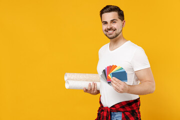 Young employee handyman man wear t-shirt hold color palette paint wallpaper rolls isolated on yellow background studio portrait. Instruments accessories renovation apartment room Repair home concept.