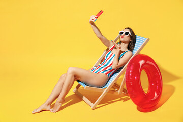 Full body length happy young woman wear red blue swimsuit sit on wooden chair hold use mobile cell phone isolated on vivid yellow color background studio Summer hotel pool sea rest sun tan concept