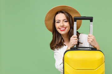 Close up cheerful fun traveler tourist woman in casual clothes hat hiding with yellow suitcase...