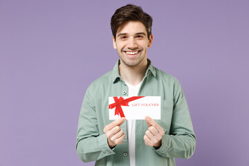 Young fun smiling excited happy caucasian man 20s wearing casual mint shirt white t-shirt holding gift voucher flyer mock up isolated on purple background studio portrait People lifestyle concept