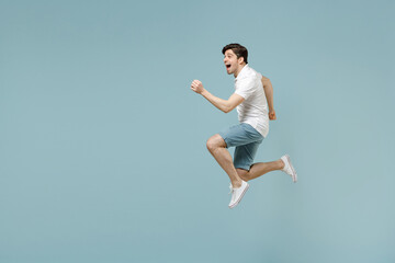 Full length young fun caucasian man 20s wear white casual basic t-shirt run fast jump high with outstretched hands isolated on pastel blue color background studio portrait. People lifestyle concept