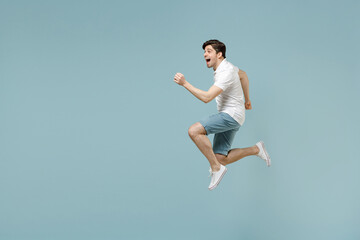 Fototapeta premium Full length young fun caucasian man 20s wear white casual basic t-shirt run fast jump high with outstretched hands isolated on pastel blue color background studio portrait. People lifestyle concept
